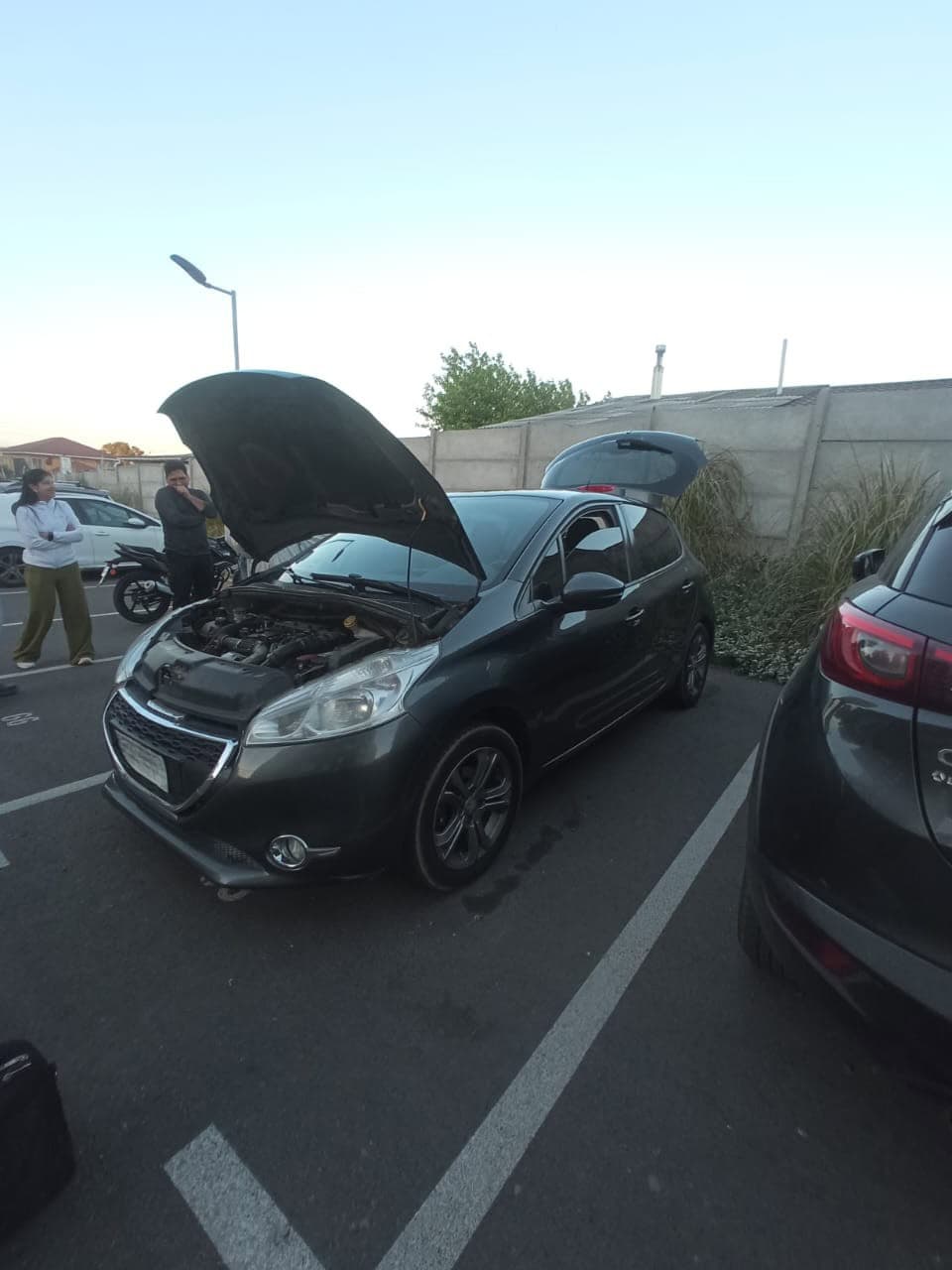 Revisión de un auto negro con el capó abierto en un estacionamiento